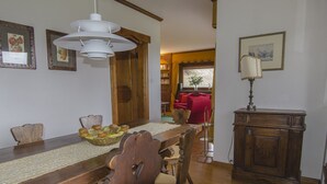 Un coin repas avec une table en bois, des chaises, un panier de fruits et un luminaire suspendu.