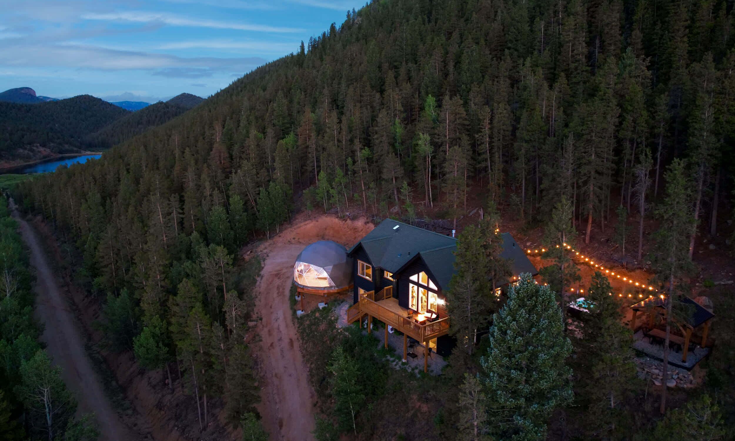 A cabin with a large dome structure, surrounded by dense forest and a dirt road.