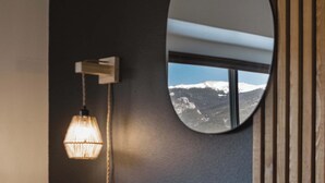 A bedroom with a bed, a round mirror, a wall-mounted lamp, and a window with a mountain view.