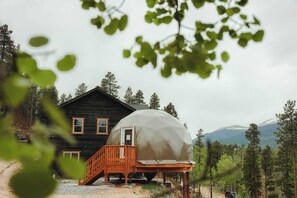 A cabin with a covered outdoor area, a wooden deck, and a view of a forested mountain range.