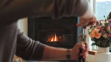 A person sitting by a fireplace with a bottle and flowers on the table.