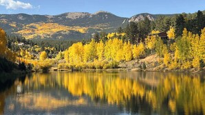 A calm lake with reflections of yellow foliage, surrounded by mountains and a clear sky.