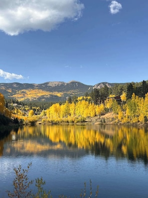 A calm lake with reflections of yellow foliage, surrounded by mountains and a clear sky.