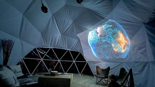 A geodesic dome interior with a projection of Earth, a seating area, and a small table.
