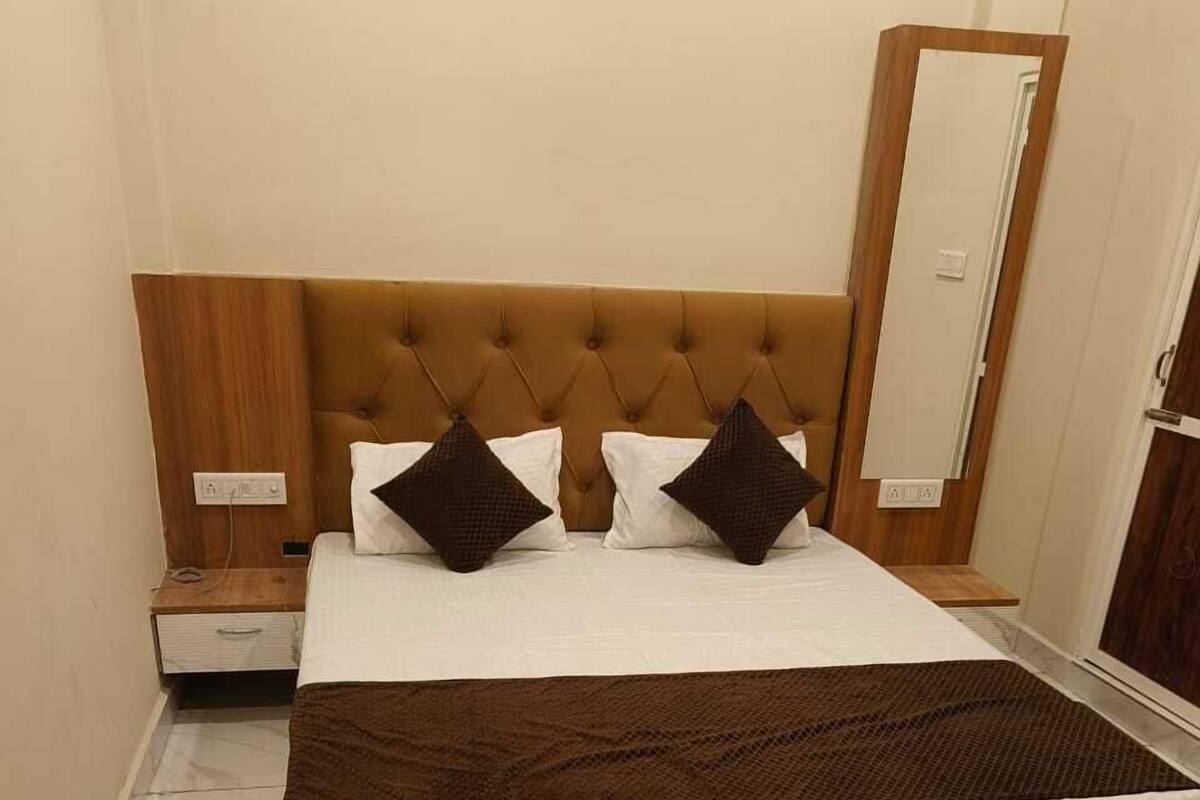 Een slaapkamer met een gestapeld hoofdbord, een houten nachtkastje, een bed met witte beddengoed en twee donkere kussens, een grote spiegel en een marmeren vloer.