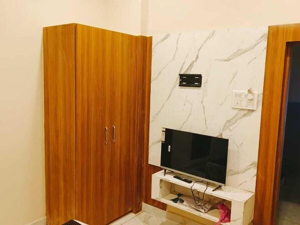 A room with a wooden wardrobe, a marble wall, and a mounted television. - Hotel Sarthak Palace (Ujjain)