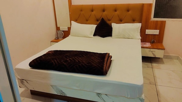 A neatly made bed with a brown blanket, white pillows, and a wooden headboard. - Hotel Sarthak Palace (Ujjain)