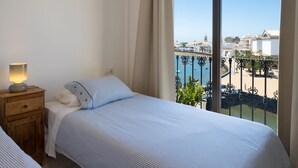 Une chambre à coucher avec un lit, une table de chevet, une lampe et une vue sur la mer et les bâtiments.