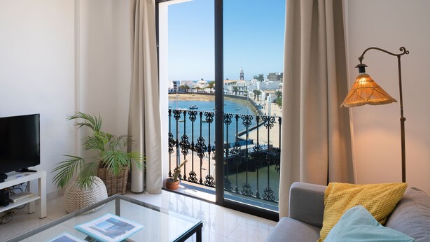 Un salon moderne doté d’une grande porte-fenêtre coulissante donnant sur un balcon, d’un téléviseur, d’une table basse et d’une lampe.