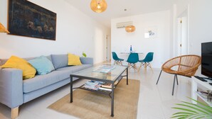 Un salon moderne avec un canapé, une table basse et des fauteuils. Un tableau est accroché au mur et un téléviseur est posé sur un meuble.