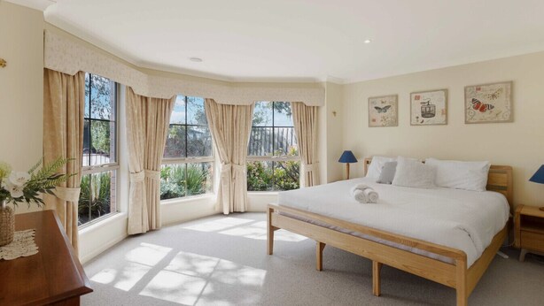Quarto com uma cama grande, mesa de cabeceira de madeira, um criado-mudo e uma janela com cortinas.