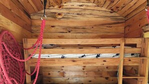 Een houten hutje met stapelbedden, een klein tafeltje en een hangmat.