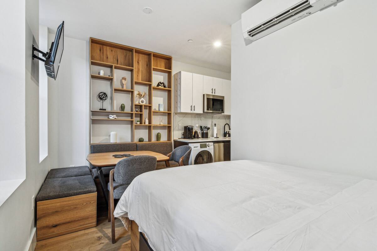 A compact room with a bed, a desk, a chair, a washing machine, and a microwave.