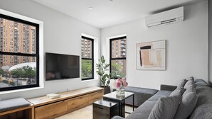 A modern living room with a large window, a flat-screen TV, a sofa, a coffee table, and a plant. - Square 42 (New York)