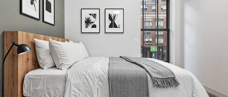 Un dormitorio moderno con cabecera de madera, ropa de cama blanca, una manta gris y cuadros en la pared.