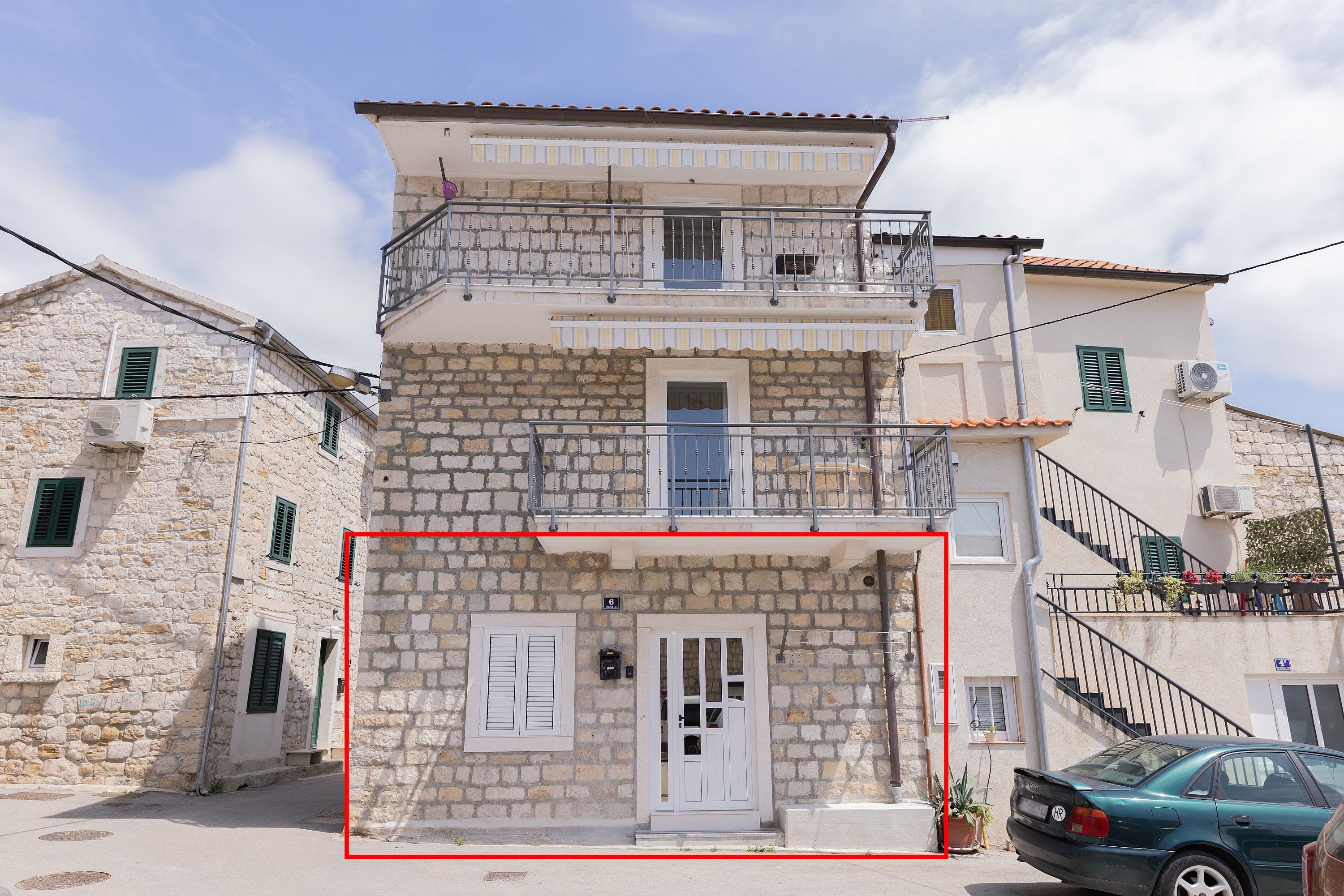 A two-story stone building with a balcony, a door, and a staircase.