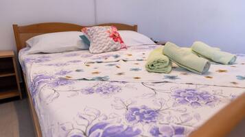 Una cama bien hecha con ropa de cama floral, una almohada y toallas enrolladas.