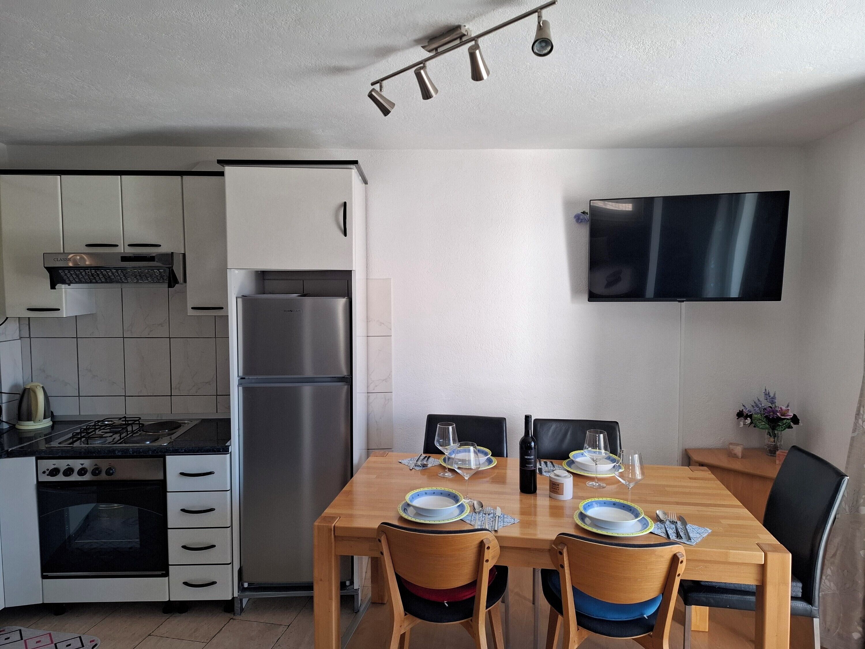 Ett modernt kök med en inbyggd ugn, ett kylskåp i rostfritt stål och ett matbord med plats för fyra personer.