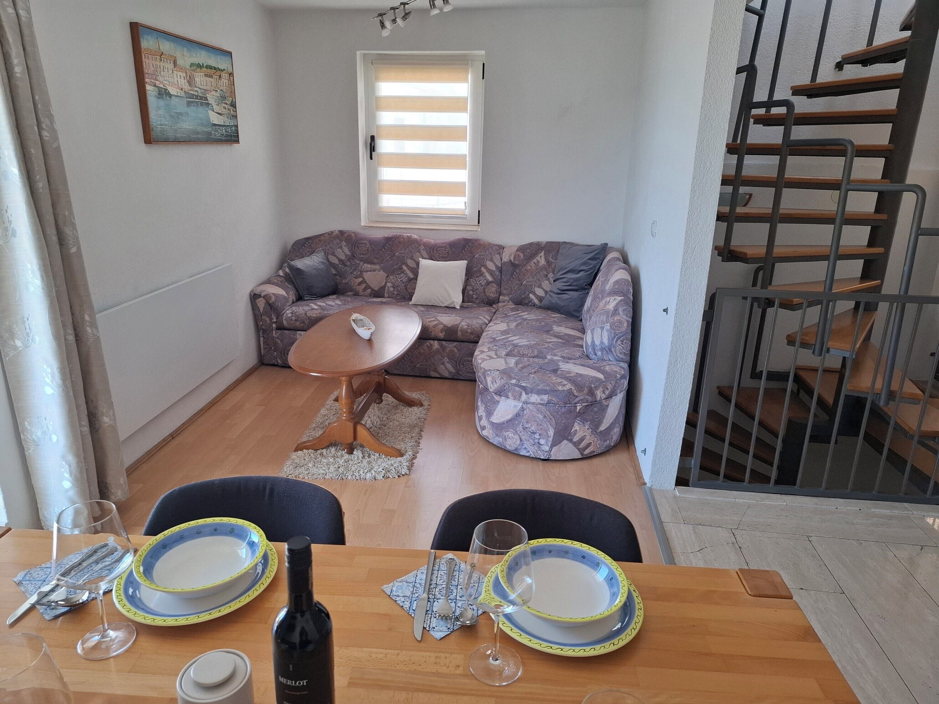 Een woonkamer met een bank, een salontafel en een eettafel, compleet met borden, bestek en een fles wijn.