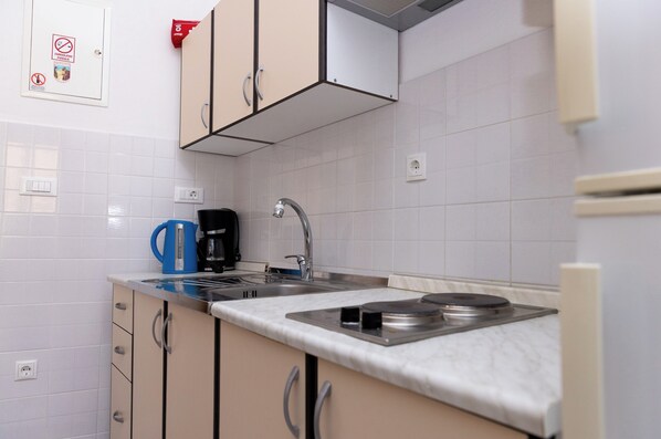 A modern kitchen with white tiles, a sink, a stove, and a coffee maker. - Apartments Kastilac with sea view (Kastel Gomilica)