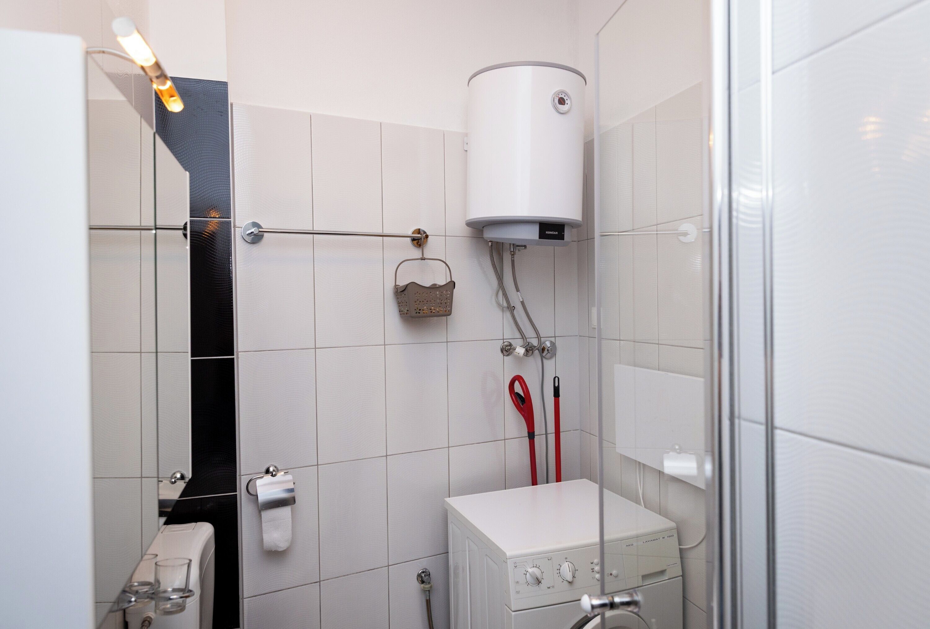 A bathroom with white tiled walls, a white toilet, a white sink, a towel rack, a showerhead, and a white heater.