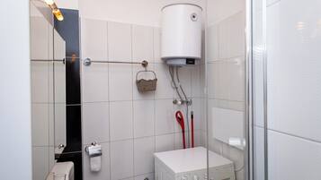 A bathroom with white tiled walls, a white toilet, a white sink, a towel rack, a showerhead, and a white heater.