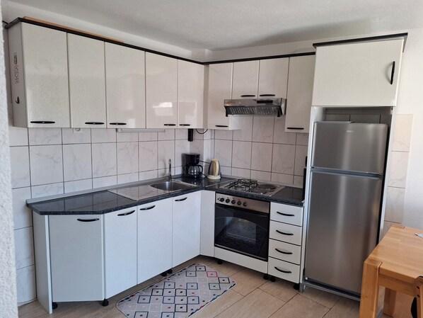 Cocina compacta con armarios blancos, refrigerador de acero inoxidable, estufa a gas y cafetera.