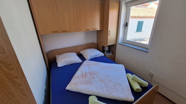 Ein kleines Schlafzimmer mit einem Einzelbett, einem Holzschrank und einem Fenster mit Blick auf Gebäude.