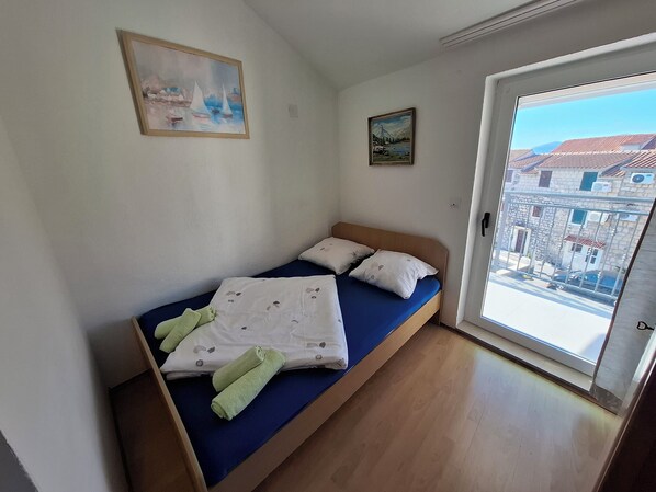 Una cama individual con colchón azul y ropa de cama blanca, un cabecero de madera y dos almohadas. Hay dos toallas verdes sobre la cama.