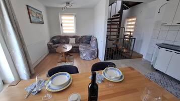 A dining area with a wooden table set for two, a bottle of Merlot wine, and a small white container.