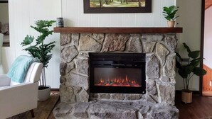 A stone fireplace with a fire, a framed picture above it, and a white wall with a wooden ceiling. - Secluded Chalet near Ohiopyle and Seven Springs (Bear Rocks)