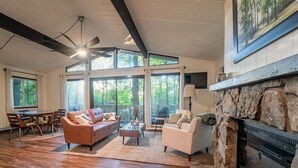 A spacious living room with a stone fireplace, large windows, and a ceiling fan. - Secluded Chalet near Ohiopyle and Seven Springs (Bear Rocks)