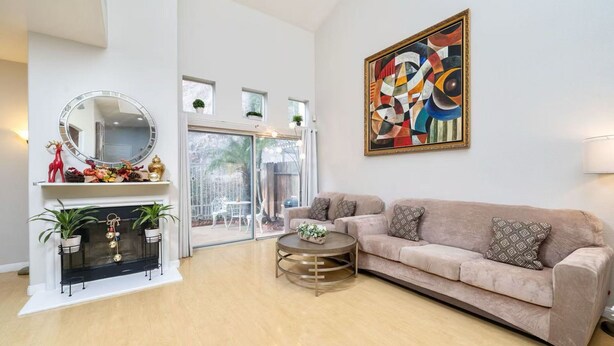 Un salon avec un canapé beige, une table basse ronde, une cheminée agrémentée de deux plantes en pot, un miroir rond et un tableau abstrait aux couleurs vives accroché au mur.