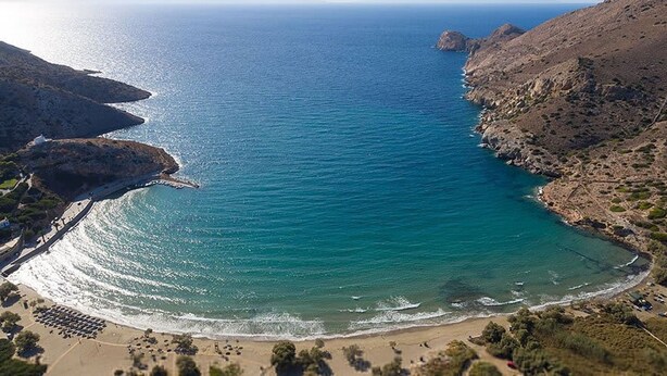 Paisaje costero con playa, acantilados rocosos y vista despejada al mar.