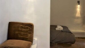 Una habitación con cama, una pequeña zona de estar y una lámpara fijada a la pared.