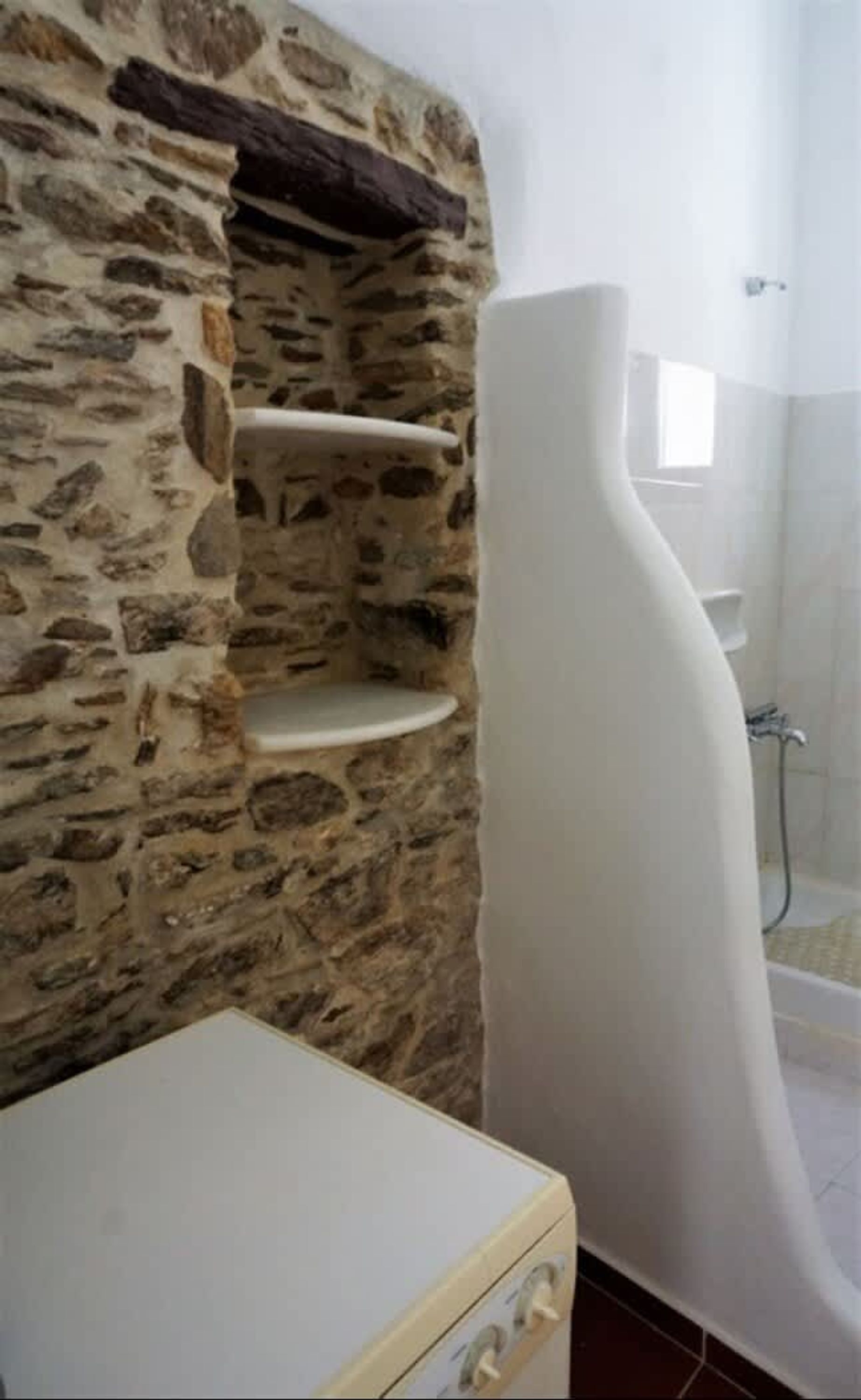 Ein Badezimmer mit Steinwand, einer weißen Badewanne und einer kleinen Ablagefläche.