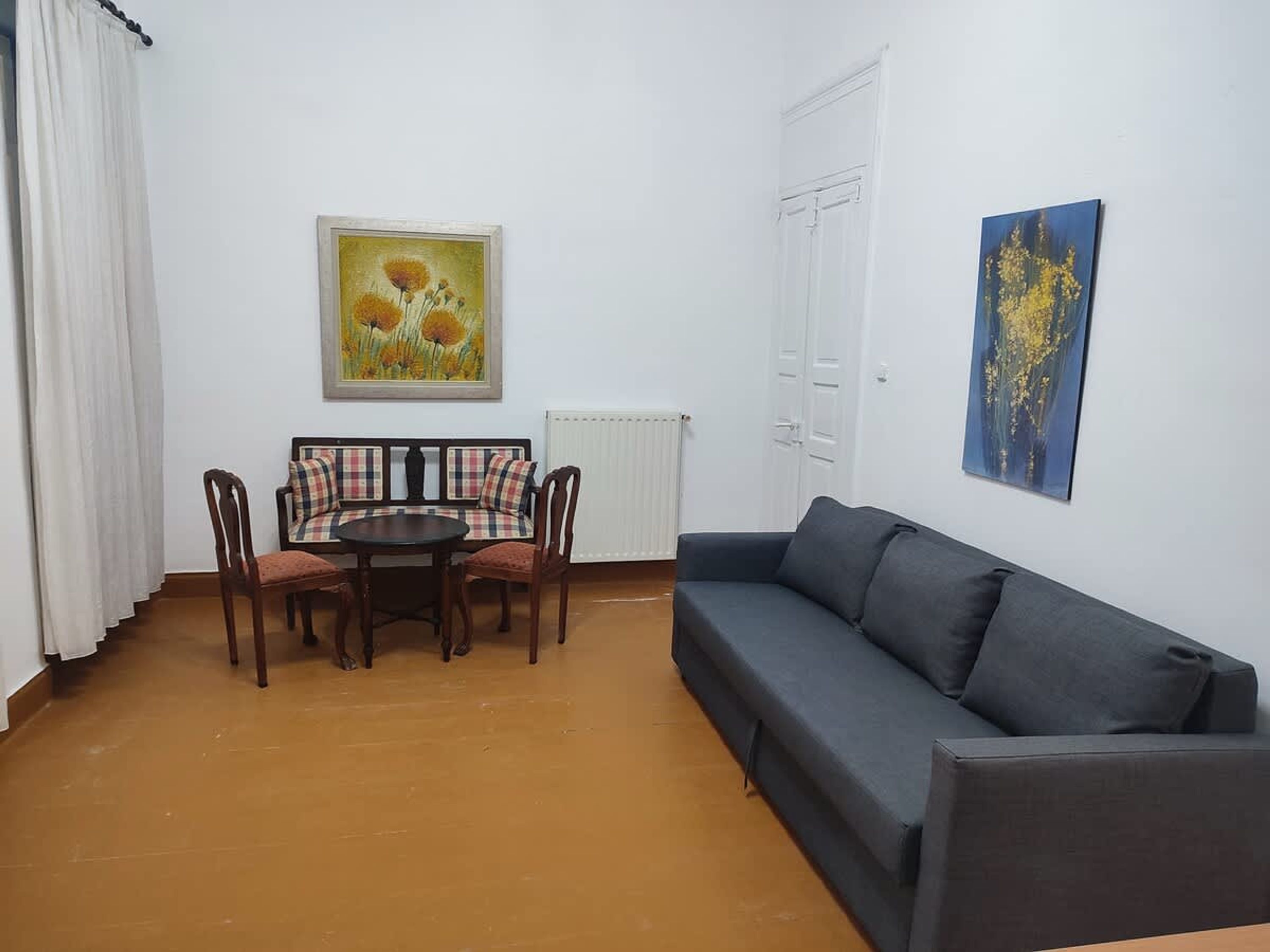 A living room with a sofa, a dining table with chairs, and two paintings on the walls.