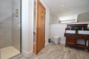 Une salle de bain avec une douche, une porte en bois, des toilettes blanches et un meuble-lavabo en bois avec un miroir.