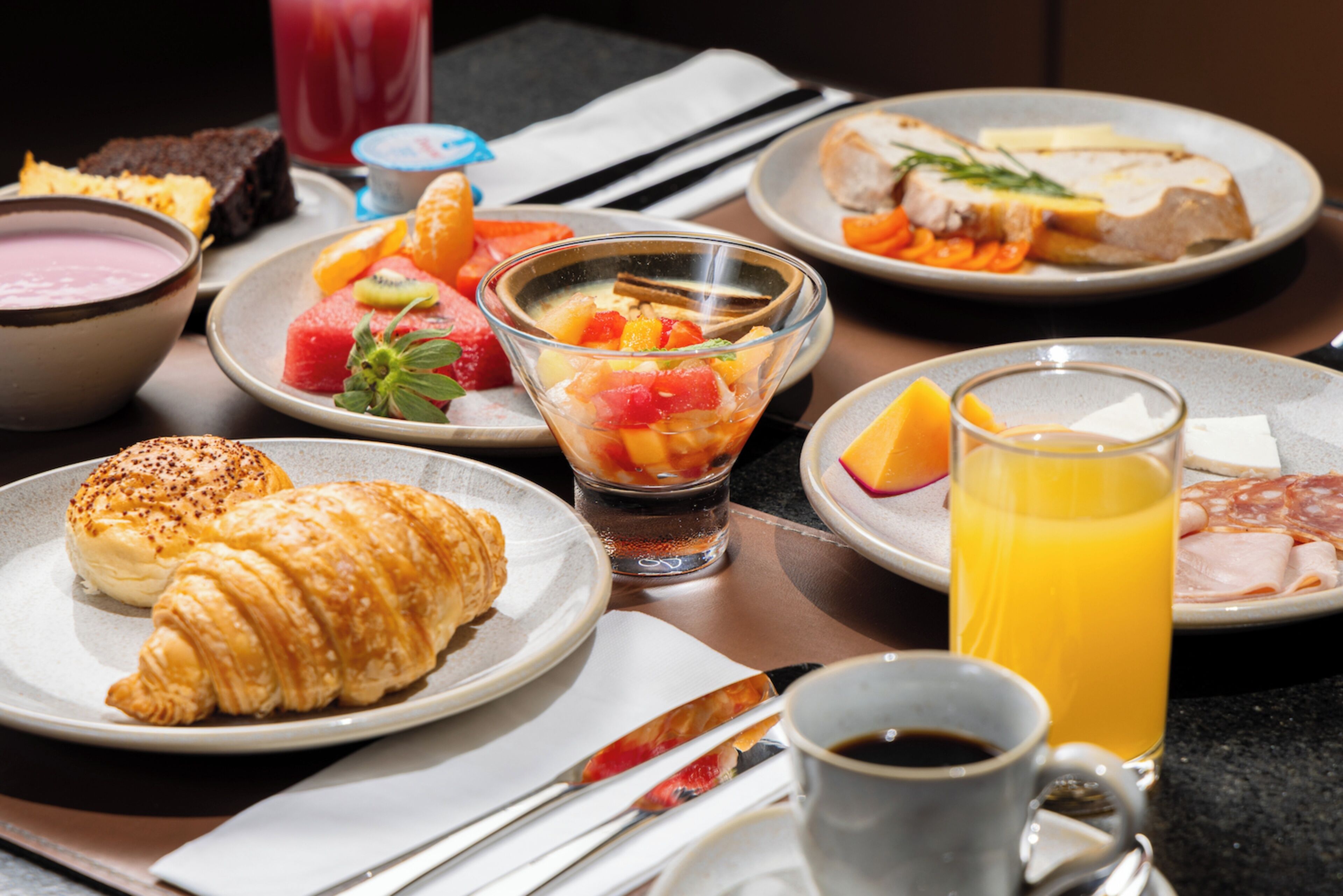 A breakfast setting with croissants, fruit, and various beverages.