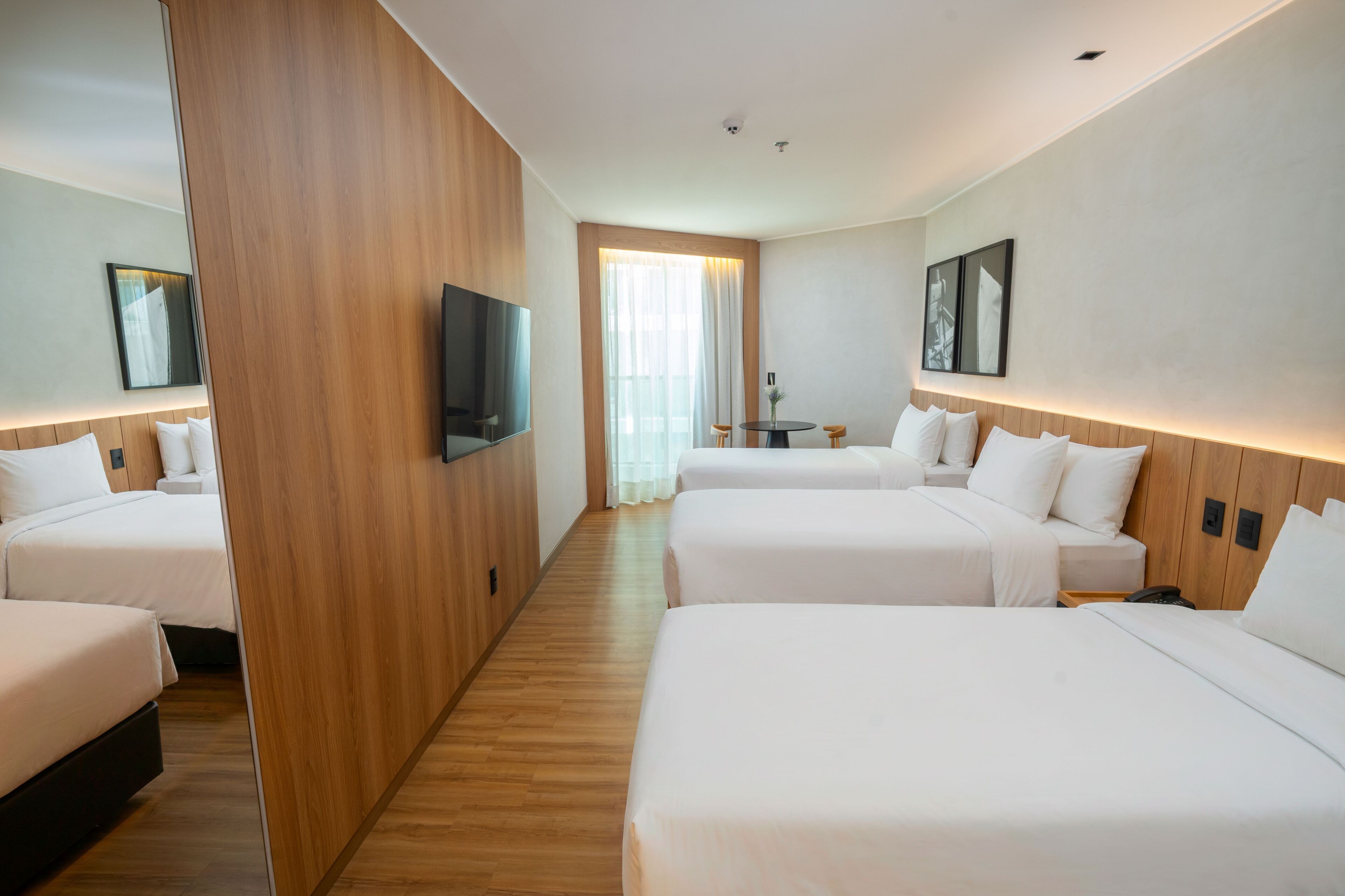 Habitación de hotel con cuatro camas, televisor, separador de madera y vistas a la ciudad.