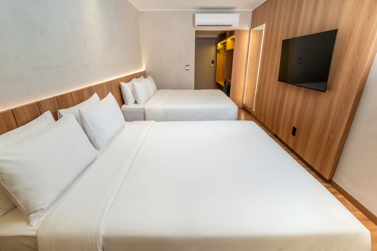 Habitación de hotel con dos camas, un televisor montado en la pared y detalles en paneles de madera.