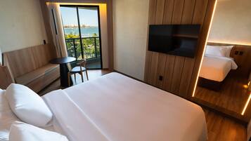 A hotel room with a large bed, a TV mounted on the wall, a small table, and a balcony with a view.