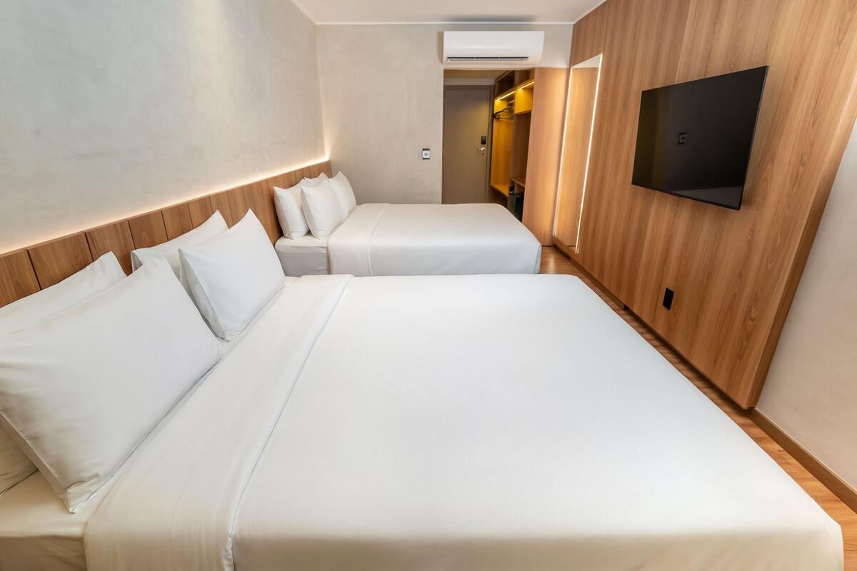 A hotel room with two beds, a TV mounted on the wall, and a wooden panel design.