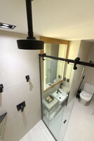 Un baño moderno con cabina de ducha de vidrio, lavamanos a la vista y un inodoro.