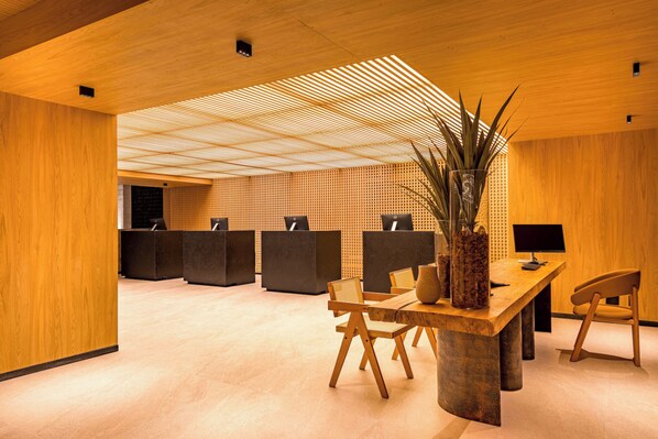 Un espace d’accueil moderne avec un lambris en bois, un comptoir d’accueil, plusieurs chaises et une grande plante en pot.