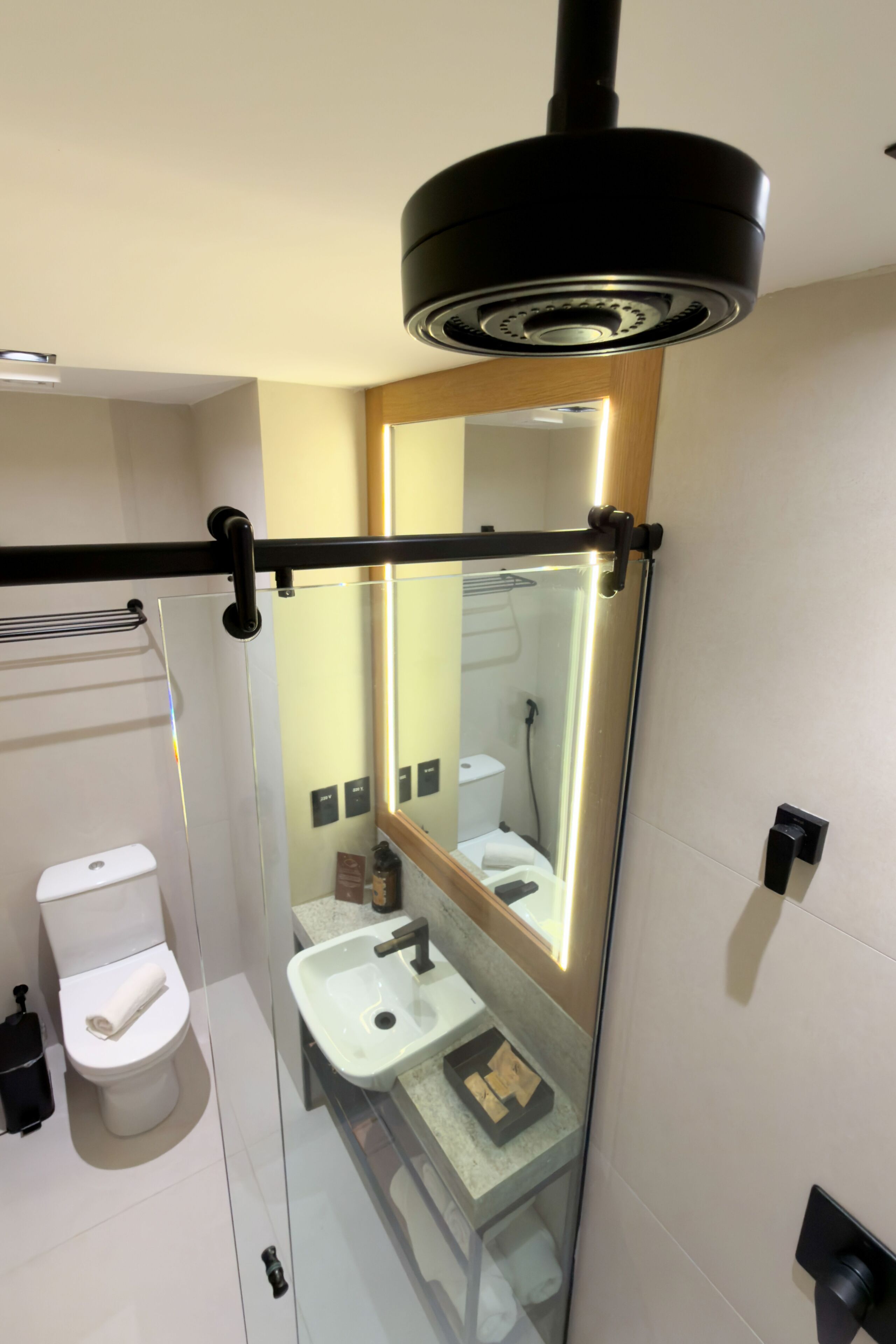 Un baño moderno con mampara de vidrio, inodoro, lavabo y espejo.
