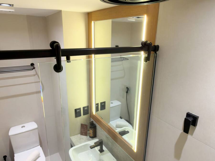 Un baño moderno con mampara de vidrio, inodoro, lavabo y espejo.
