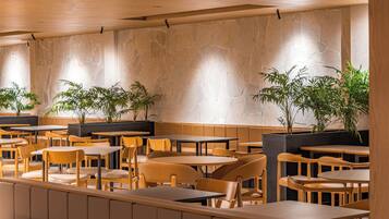 A restaurant interior with wooden tables and chairs, stone walls, and potted plants.