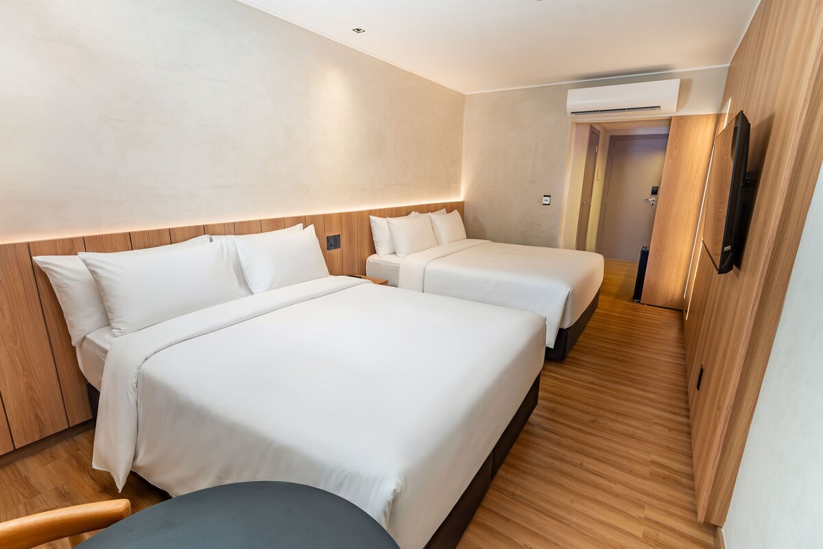 Habitación de hotel con dos camas, suelo de madera, televisor de pantalla plana y aire acondicionado.