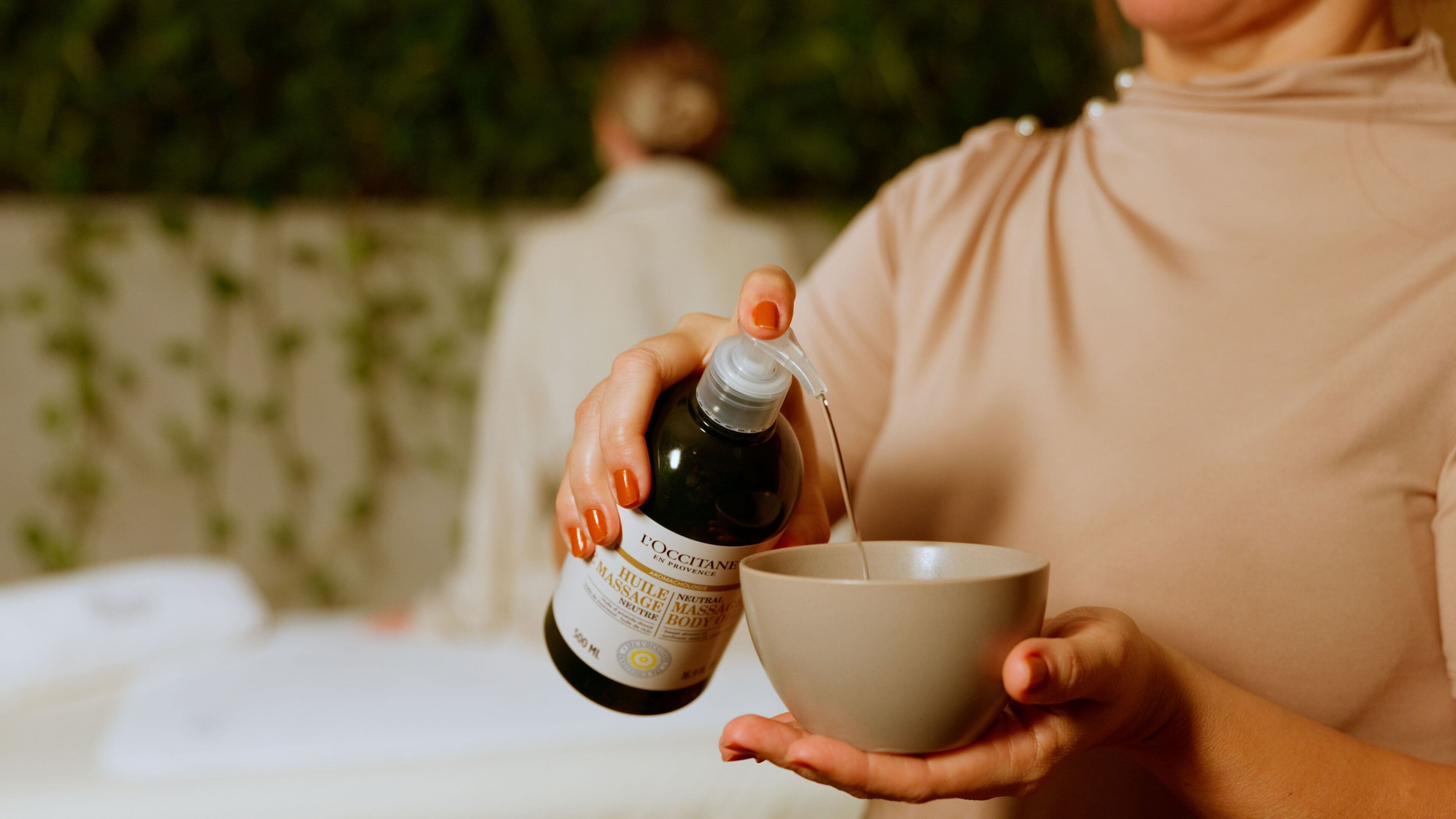 A person holding a bottle and pouring a liquid into a bowl.